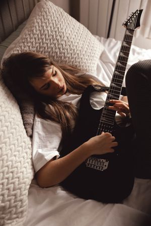 Young brunette woman playing guitar on bed