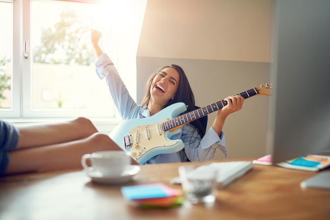 Happy woman playing guitar at her desk