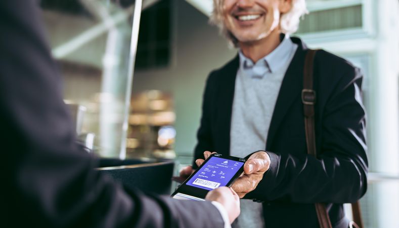 Businessman showing plane boarding pass to staff on mobile phone