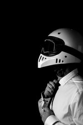 Stylish driver in helmet and eyeglasses adjusting tie in studio
