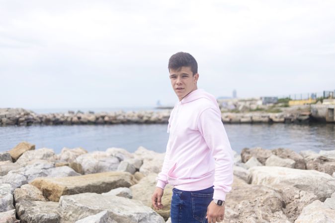 Young male teenager standing on rocky breakwater and looking at camera with copy space
