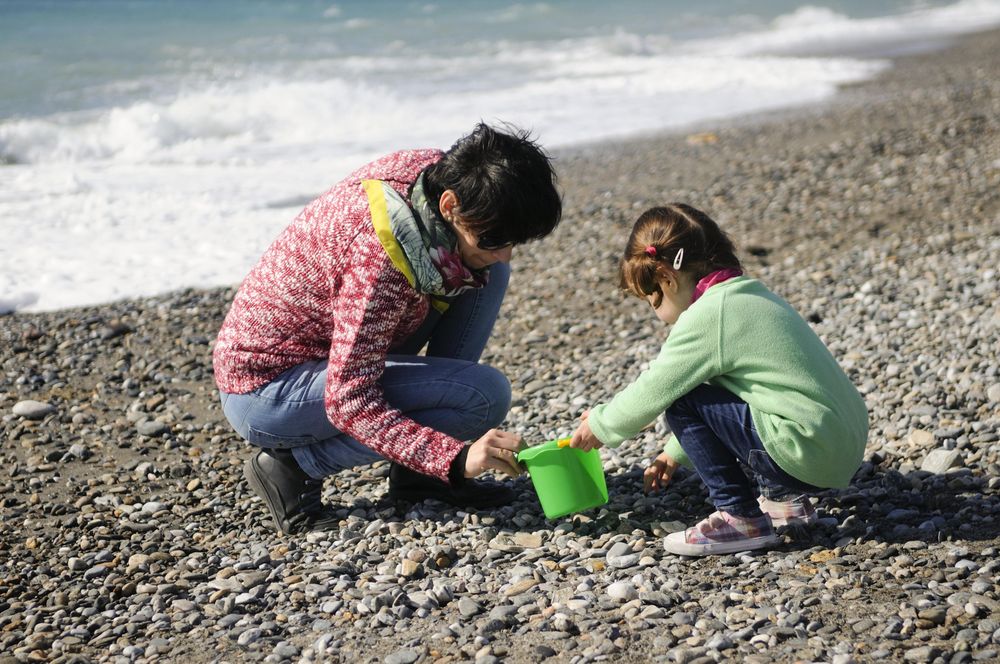 Woman and girl collecting rocks on a cold beach