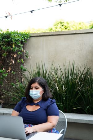 Woman in face mask working on a laptop at an outdoor table