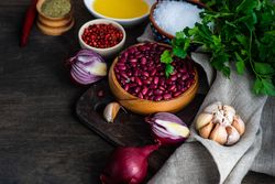 Bowl of dried kidney beans surrounded by onions, garlic, peppercorn, salt, oil and parsley with copy space