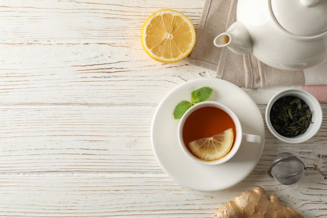 Cup of tea with lemon, mint, strainer, ginger and teapot on wooden background, top view