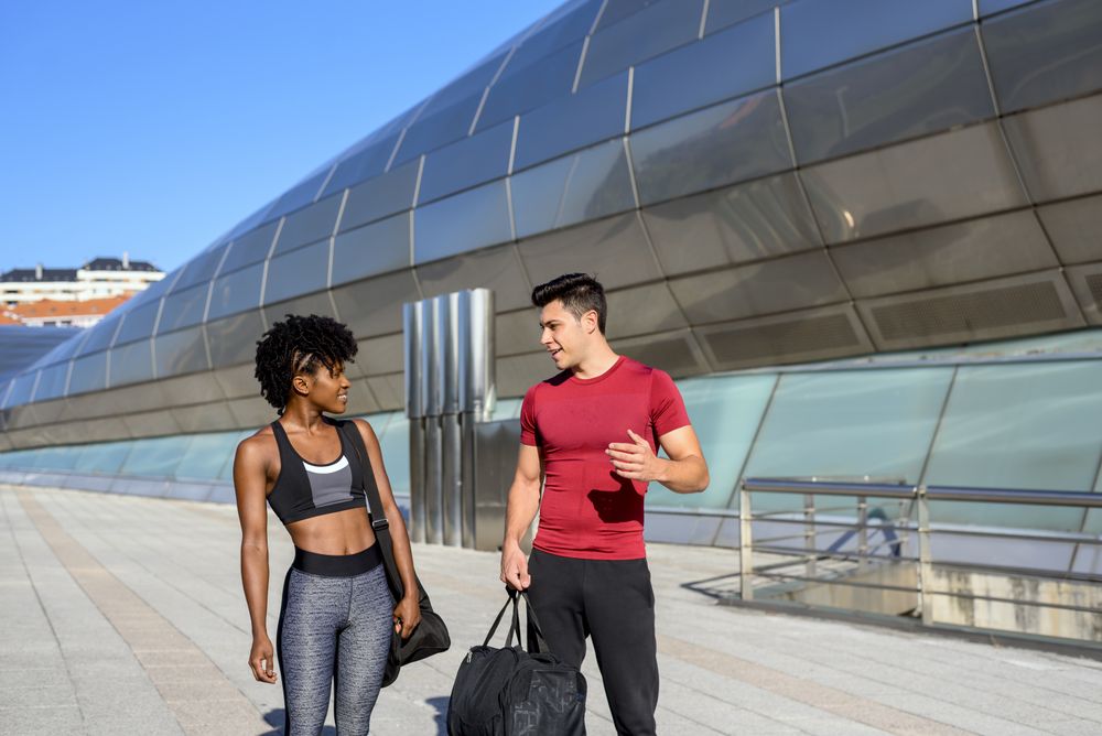 Happy sportive man and woman walking along wall in city