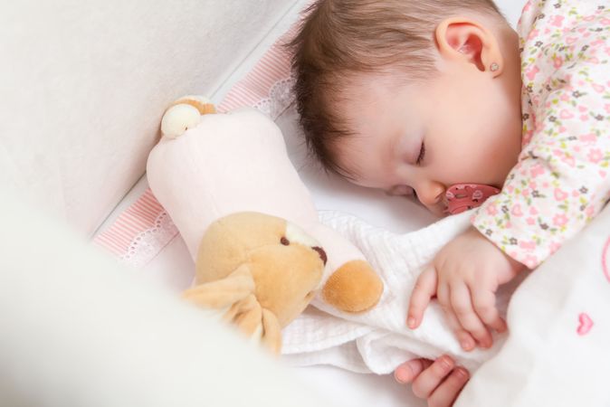 New born baby girl sleeping in a cot with pacifier and toy