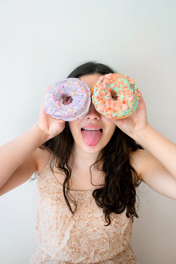 Playful woman making glasses of donuts while standing by white wall
