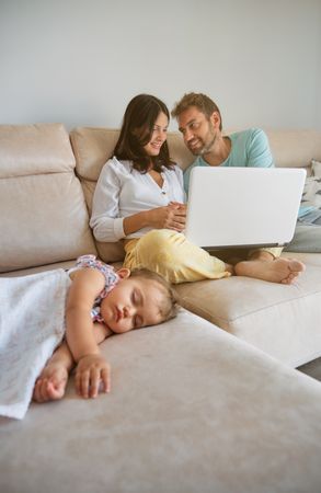 Mother and father browsing laptop near sleeping daughter