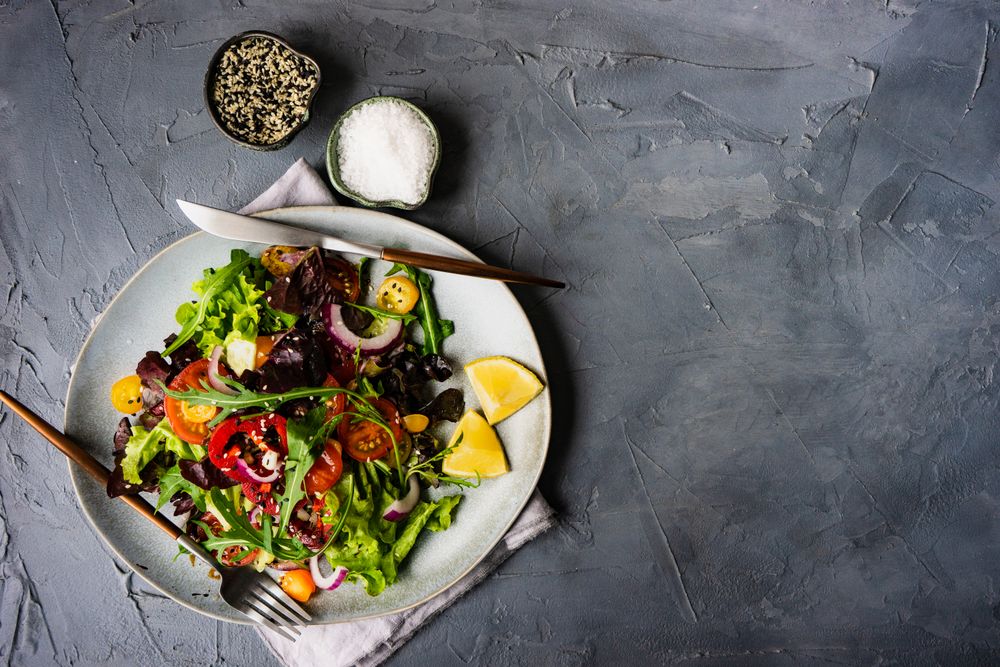 Top view of organic vegetable salad with side of salt and sesame seeds and space for text