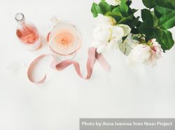 Glass of pink rose wine, and bottle with flowers and ribbon, horizontal composition with copy space 4NYgD5