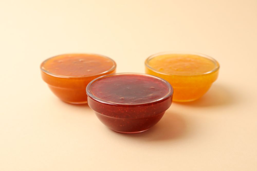 Bowls with jam on beige background, space for text