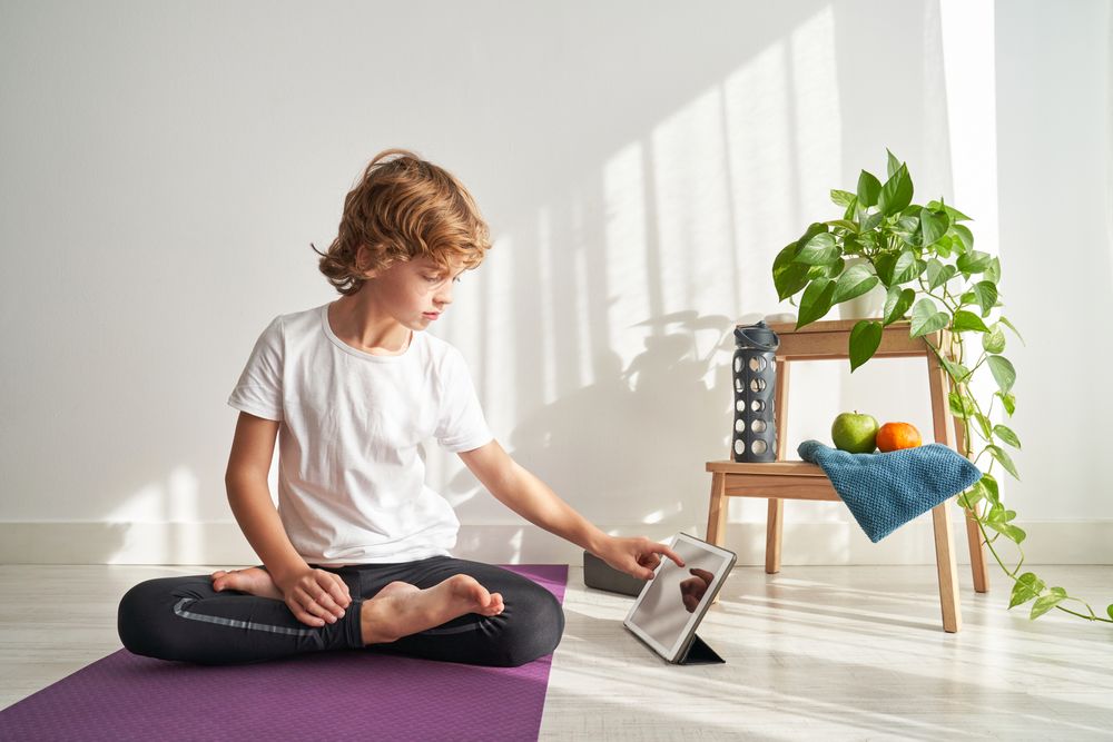 Focused preteen boy sitting in Lotus pose and browsing tablet