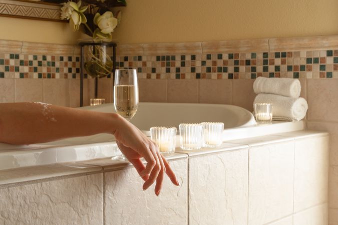 Woman Relaxing in the Bathroom Spa Tub with a Glass of Sparkling Champagne and Candles.