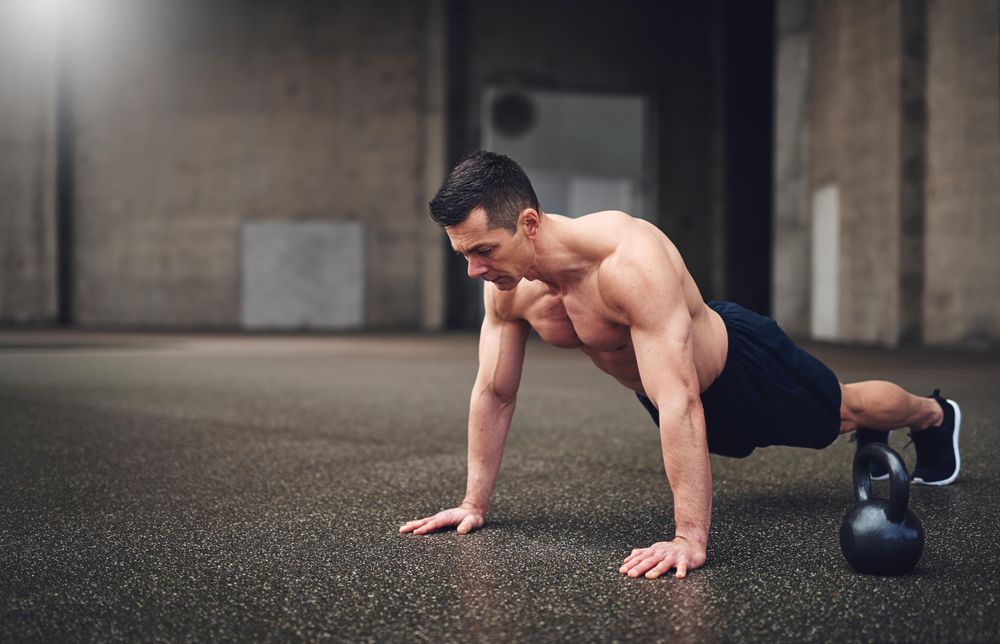 Muscular man doing plank next to kettlebell