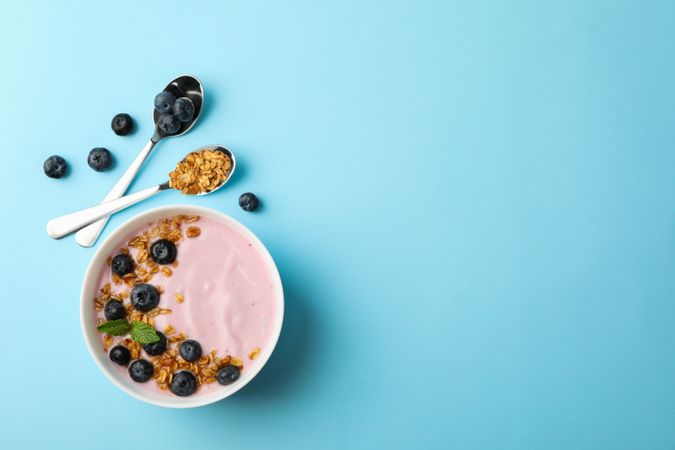 Yogurt with granola, blueberry and mint on color background