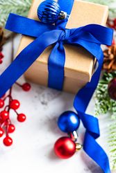 Top view of present wrapped in blue bow with holly, baubles and pine