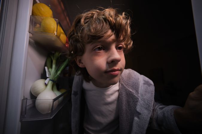 Boy standing near opened fridge at night