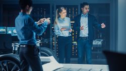 Shot of a Development Laboratory Room with Diverse Professional Team of Engineers and Scientists Working on a Electric Car Chassis with Wheels, Batteries, Engine and Suspension.