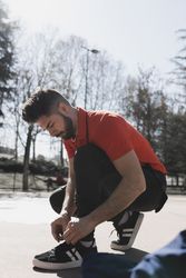 Handsome man lacing shoes in park