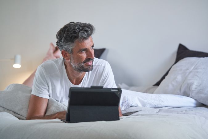 Positive man with tablet in bedroom