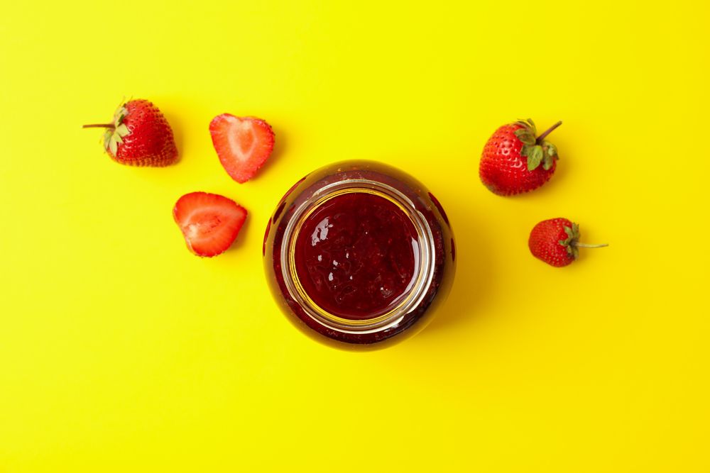 Delicious strawberry jam on yellow background, top view