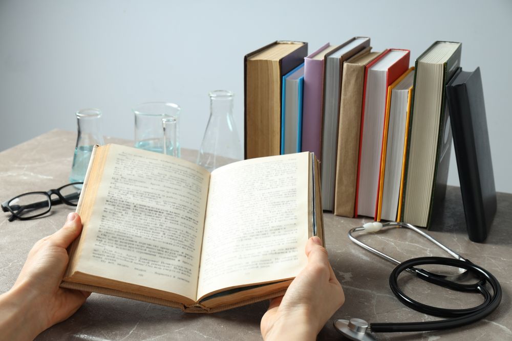 Books, stethoscope, flasks and hands on gray background