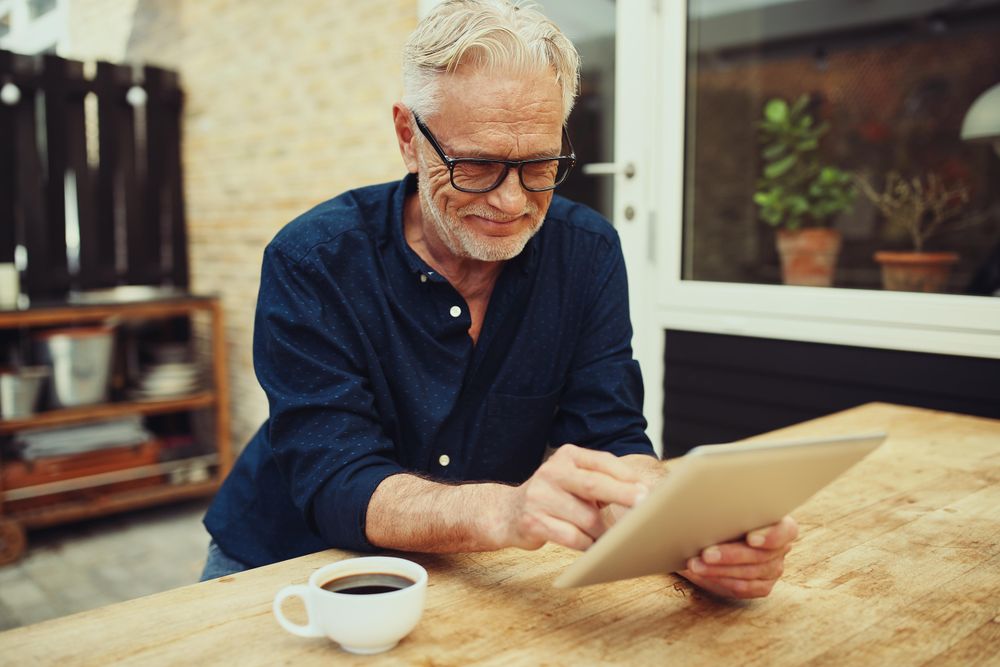 Man reading his tablet outside with a cup of coffee