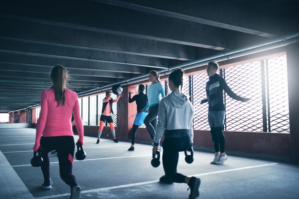 People doing circuit training in a covered park lot with sun coming through windows