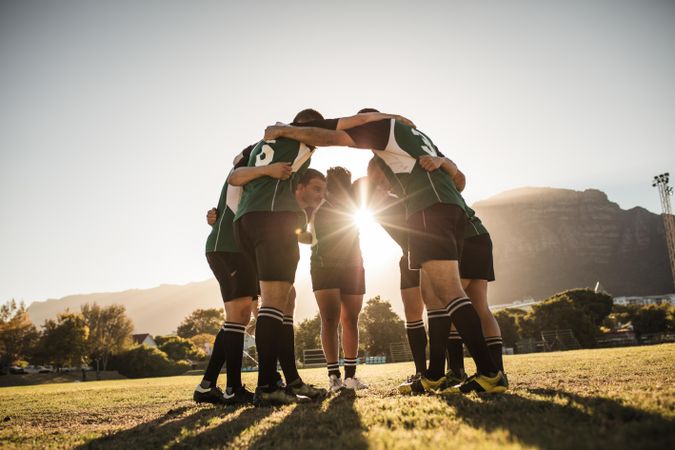 Rugby players standing in a circle with their hands on shoulders