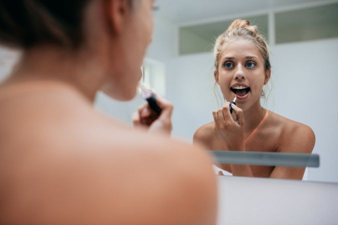 Reflection of woman in the mirror while applying lipstick
