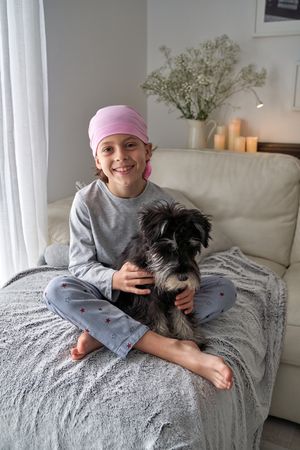 Happy boy in pink bandana stroking purebred dog on sofa