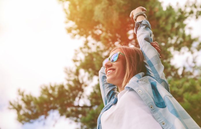 Woman with sunglasses raising her arms over nature background