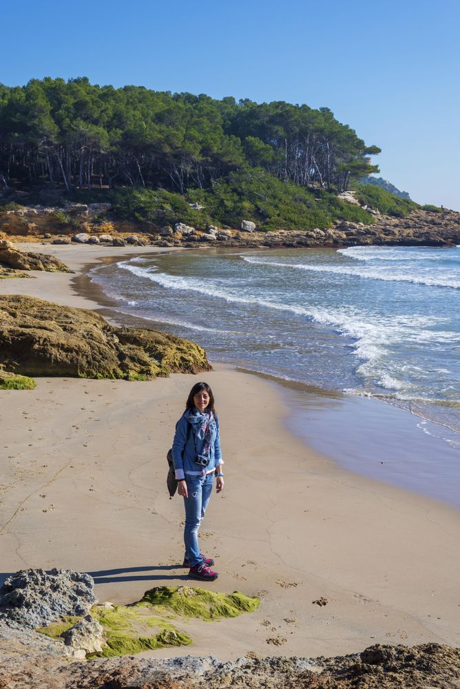 Female dressed in blue standing on the beach looking up at the camera