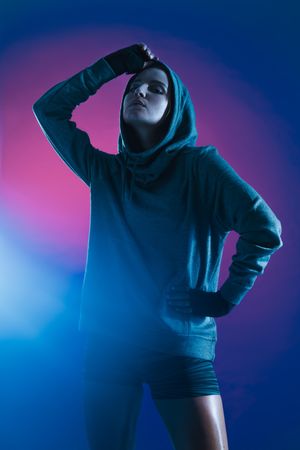 Sporty woman wearing a hooded sweatshirt on colored background
