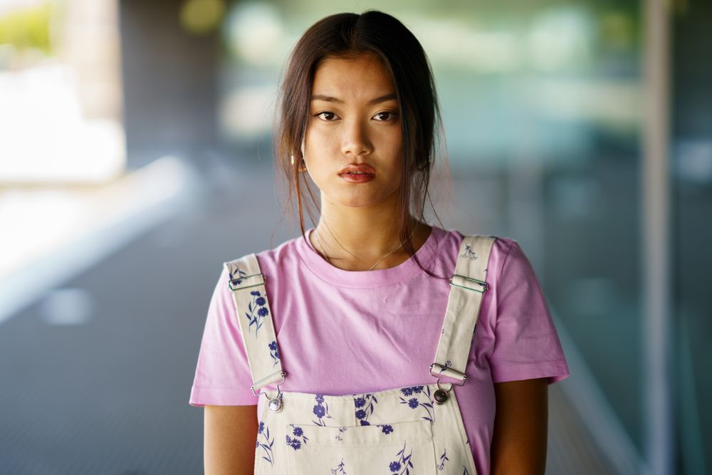Chinese female in floral overalls and pink t-shirt looking at camera outside