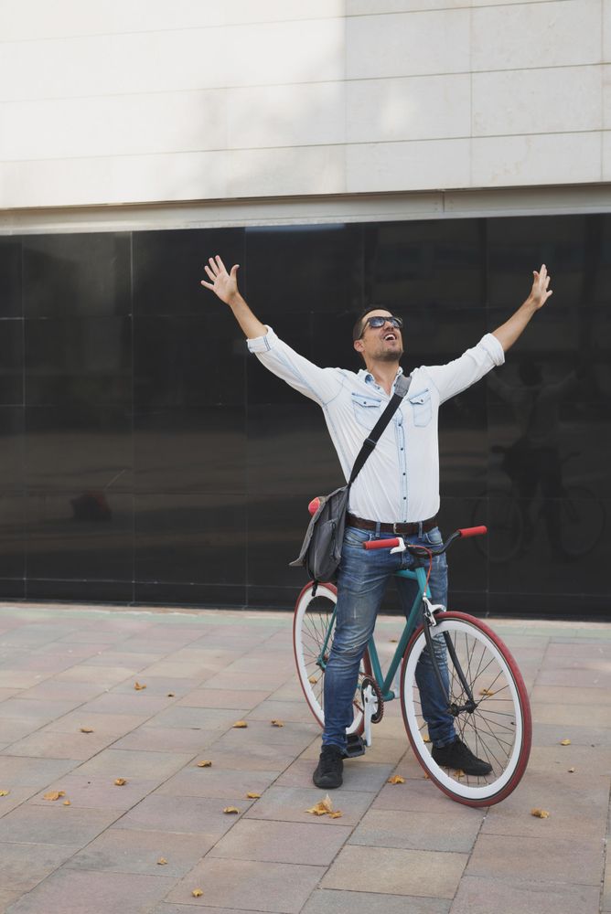 Male sitting on colorful bicycle with both arms up and outstretched