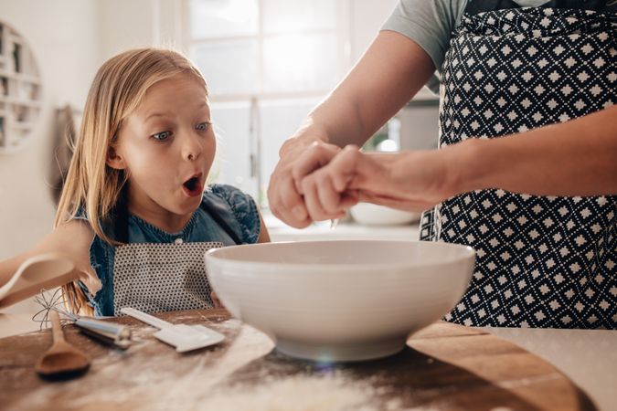 Surprised young girl watching egg getting cracked in bowl
