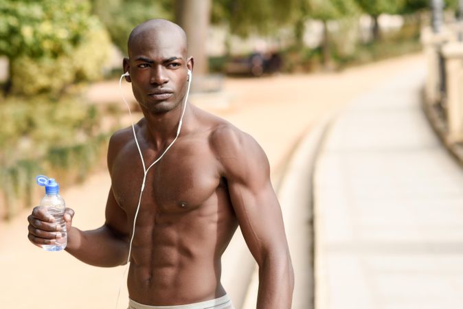 Athletic male with shirt off drinking from a water bottle in an outdoor park