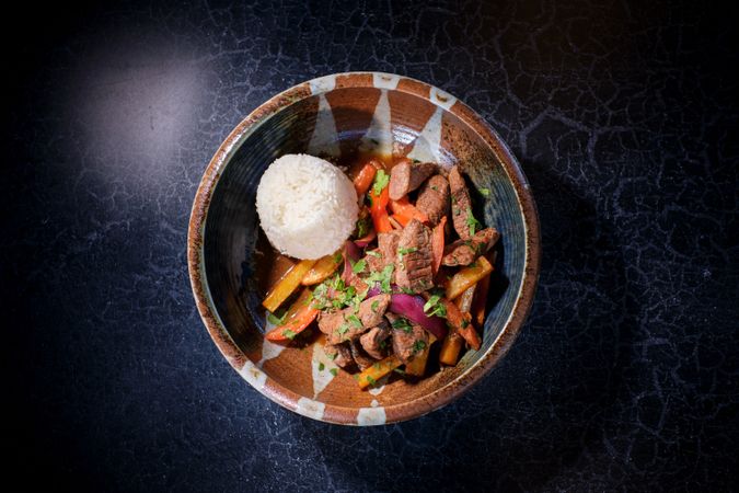 Bowl with delicious fried beef with vegetables and rice on black table