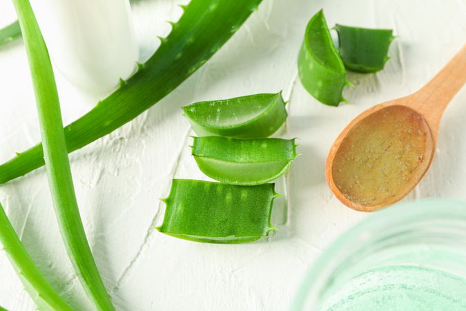 Spoon with cream, aloe vera leaves and slices on table, closeup. Natural treatment