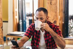 Black man using smartphone while having coffee at home