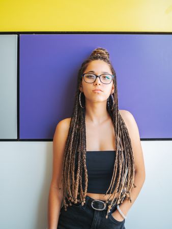 Charming teenage girl with braids in sunglasses nearby colorful wall
