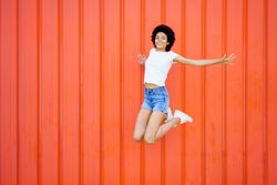 Woman in shorts and t-shirt jumping with knees bent against red wall