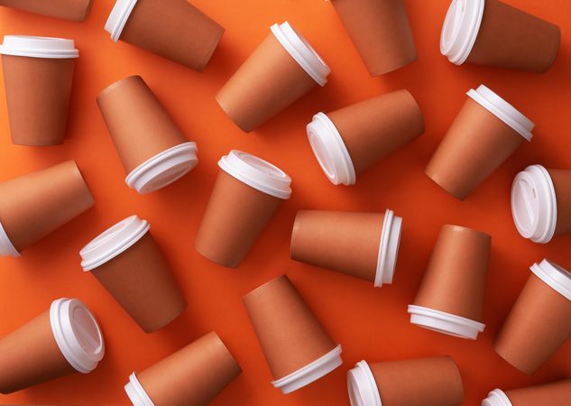 Scattered disposable coffee cups on orange background