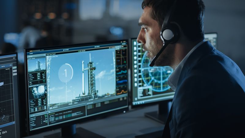Aerospace Engineer Monitors Rocket Launch Countdown on Multiple Screens.