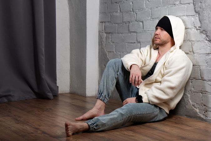 Barefoot man in fleece jacket and jeans sitting on floor.