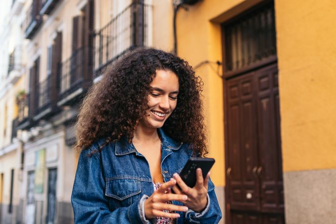Cheerful Black Latina woman using smartphone outdoors