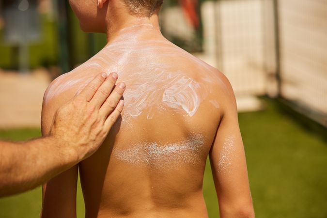 Faceless man applying sun cream on kid