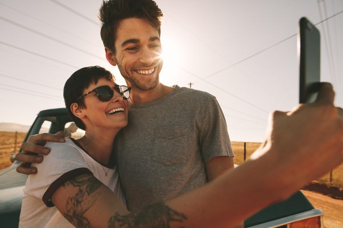 Couple pose for selfie holding each other with evening sun in the background